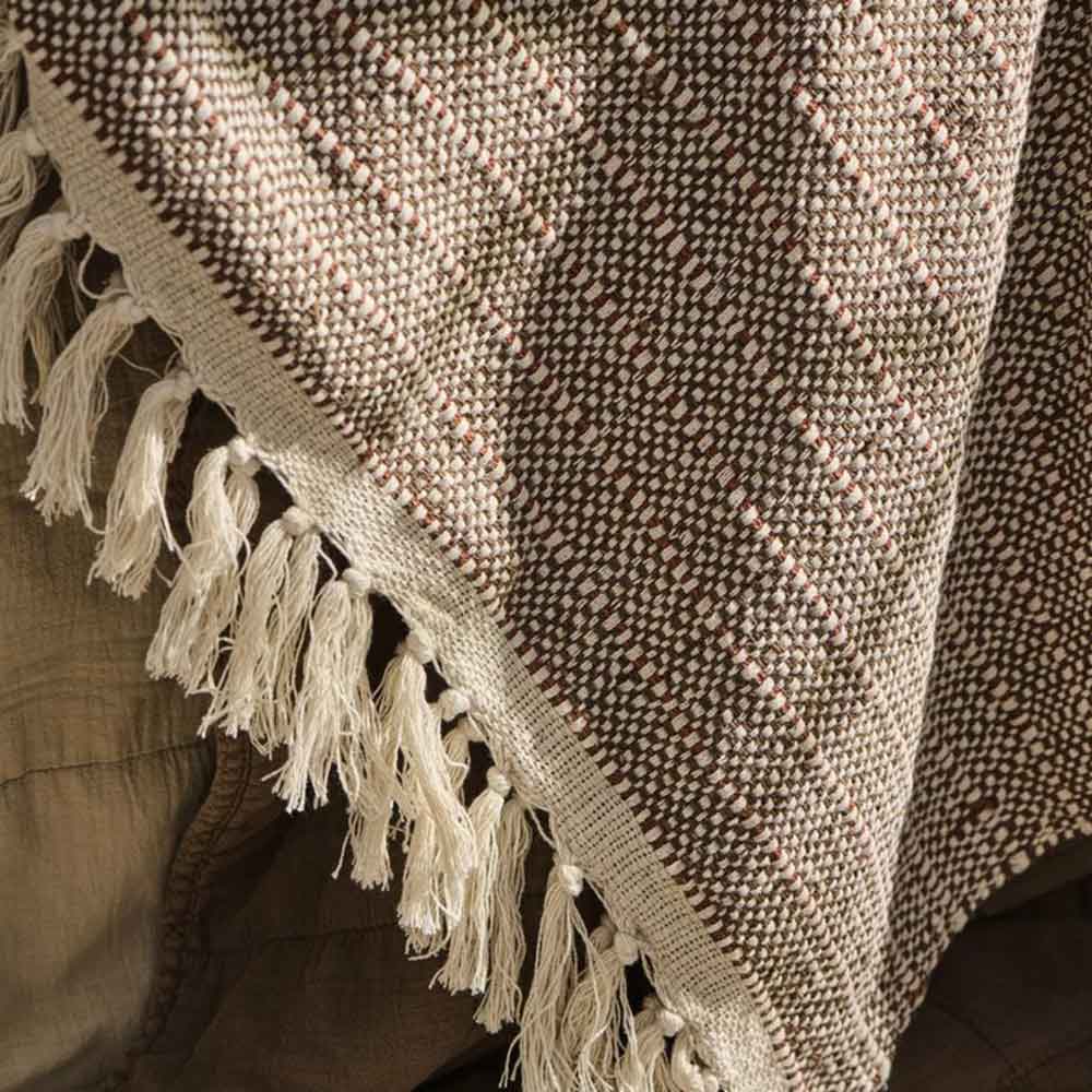 Nahaufnahme eines Plaids mit braunen und naturfarbenen Webstreifen sowie hellen Fransen auf Holz
