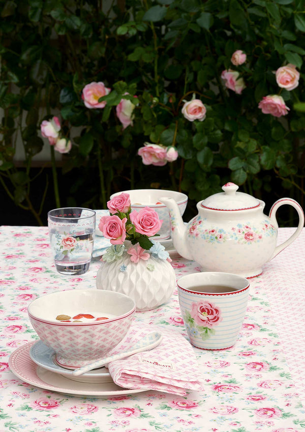 Kleiner Teetisch mit rosa GreenGate-Geschirr und Stoffserviette vor blühenden Rosen