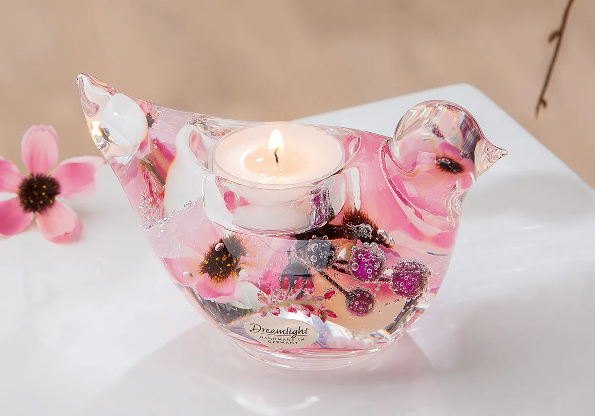 Dreamlight Teelichthalter in Vogelform mit rosa Blütendekor und brennendem Teelicht auf einem hellen Tisch