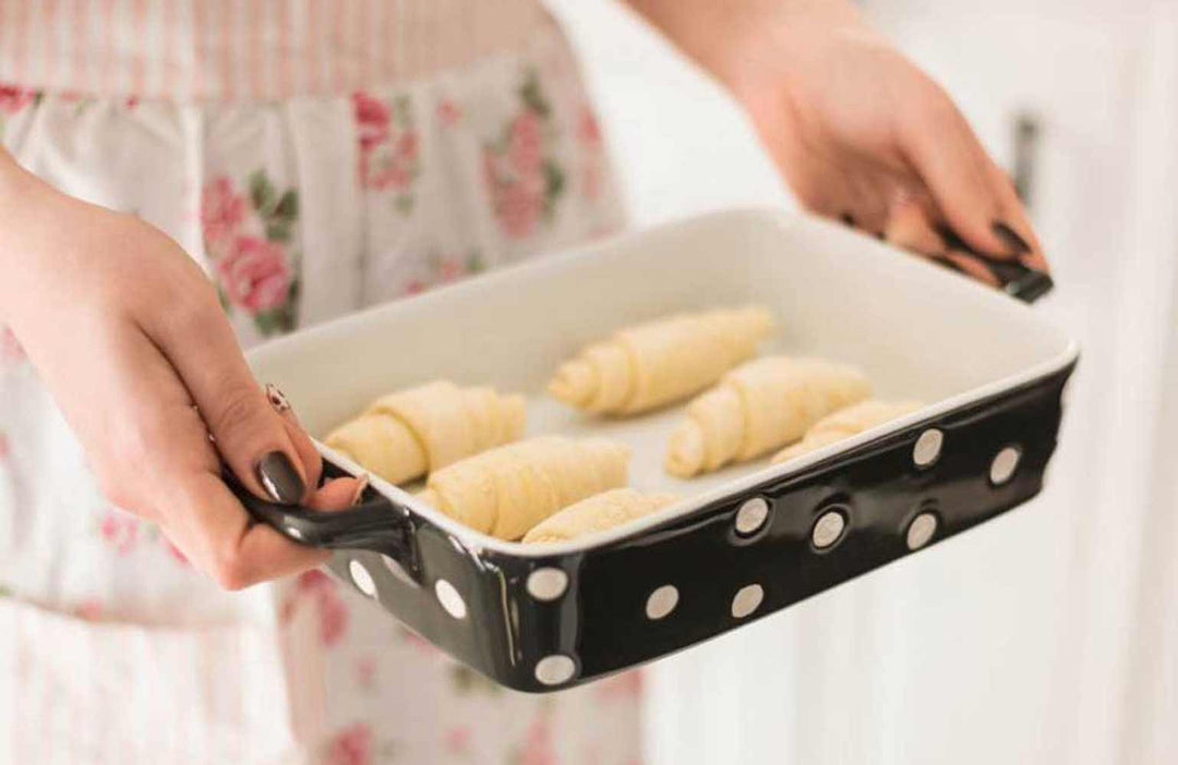 Eine Person hält eine schwarz-weiß gepunktete Auflaufform mit ungebackenen Croissants.