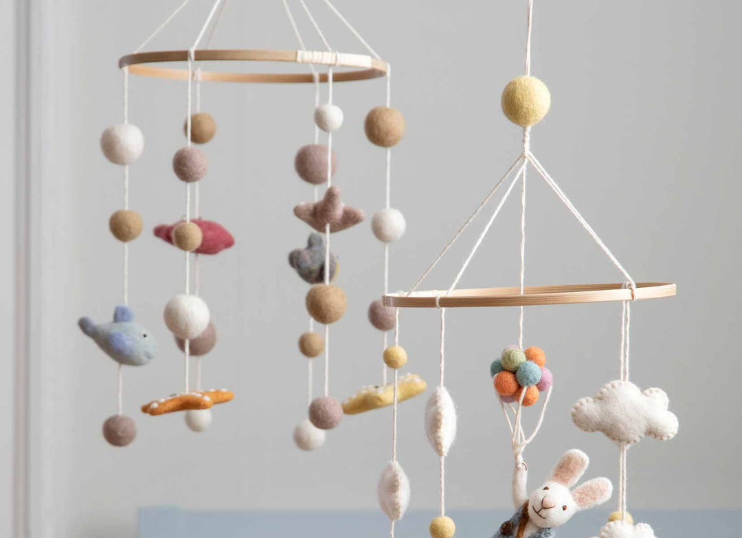 Ein farbenfrohes Baby-Mobile aus Filz mit Tieren und Bällen, die vor einem hellen Hintergrund an einem Holzreifen hängen.