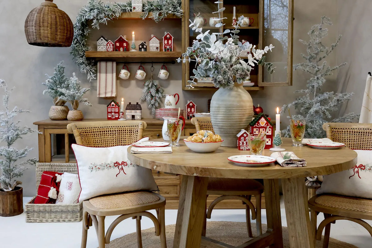 Weihnachtliche Chic-Antique-Wohnszene mit Schleifenkissen, roten und weißen Textilien und gedecktem Holztisch