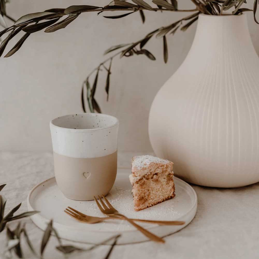 Eulenschnitt Becher Herz mit Kuchenstück auf einem hellen Teller neben einer Vase