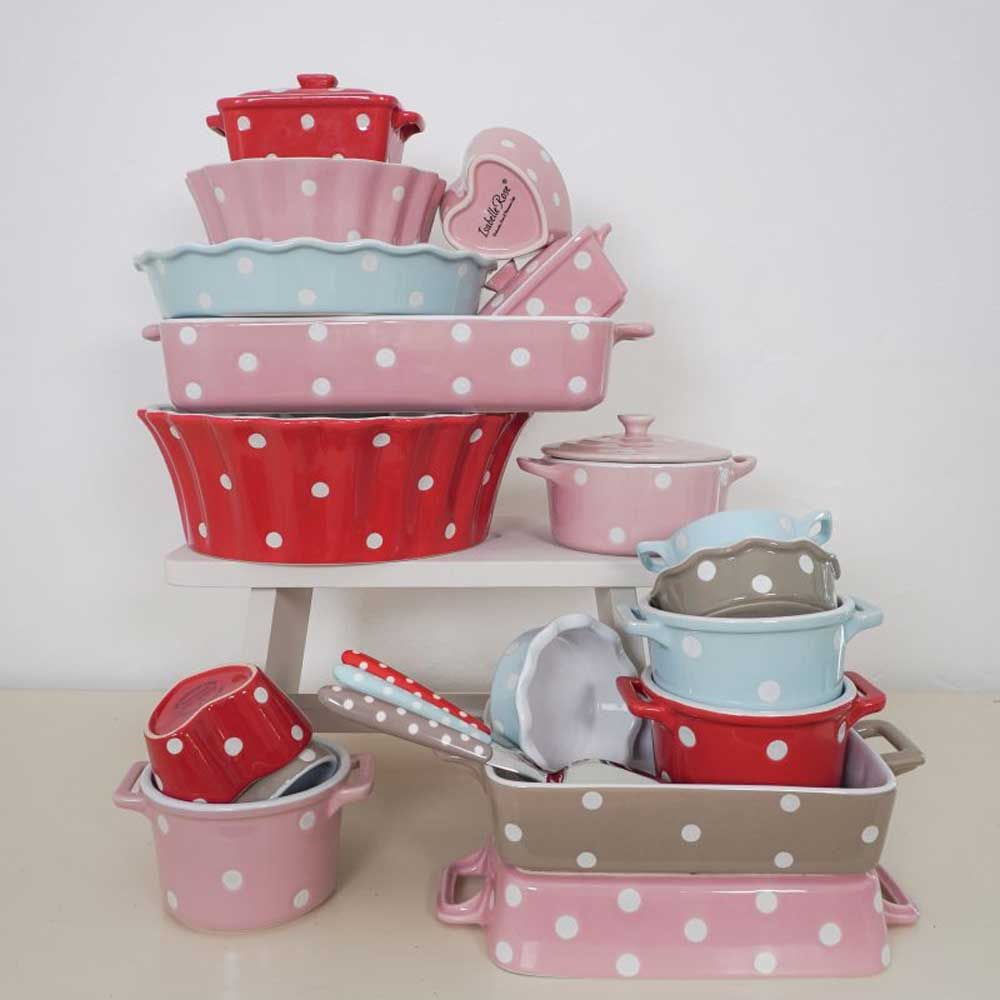 Eine Sammlung gepunkteter Keramik-Auflaufformen, Schüsseln und Utensilien in Rosa, Rot, Blau und Beige sind auf einem weißen Etagenregal gestapelt.