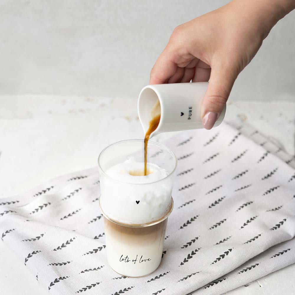 Milchkanne gießt Milch in Latte Glas