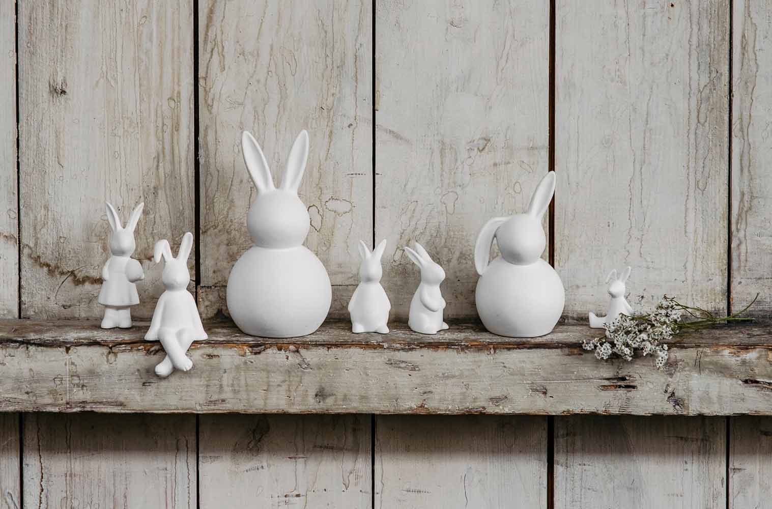 Auf einem Holzregal steht eine Gruppe weißer Hasenfiguren.