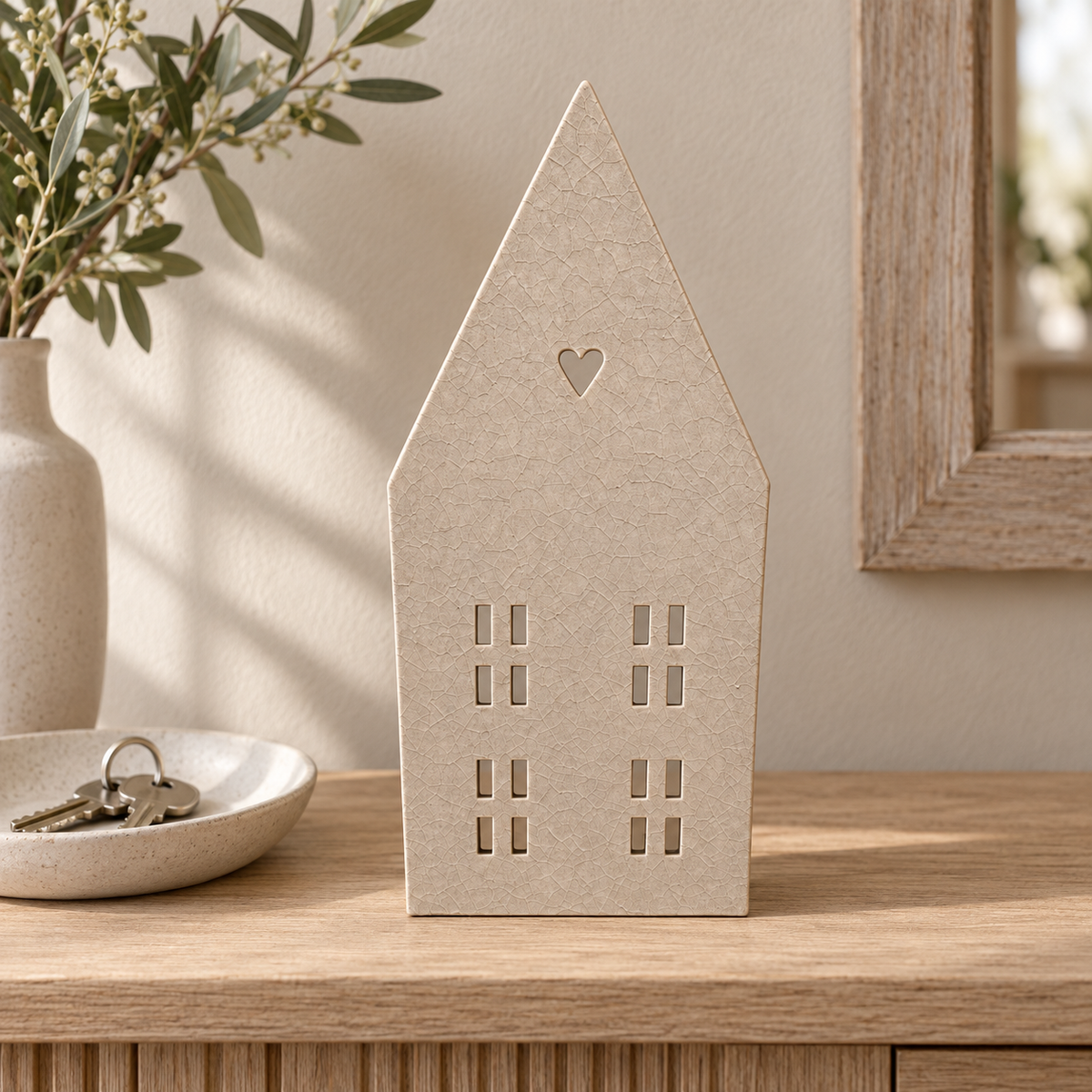 Beiges Dekohaus mit Herzausschnitt und Fensteröffnungen auf einer Holzkonsole neben Vase und Schlüsselschale
