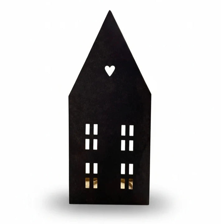 Das Alsaba Home - Lichthaus für Kerzen aus Metall in Schwarz-Gold ist eine schwarze Laterne in Form eines Metallhauses mit einem Herzausschnitt in der Nähe des Daches und rechteckigen Fensterausschnitten auf der Vorderseite.