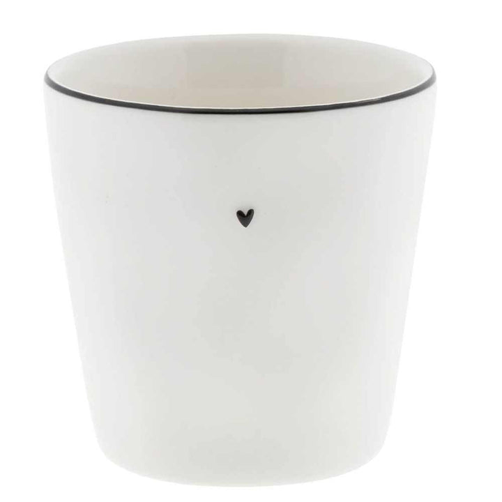 Der Becher Natural Shape der Bastion Collections ist eine weiße Keramiktasse mit einem kleinen schwarzen Herzdesign auf der Vorderseite und einem schwarzen Rand oben.