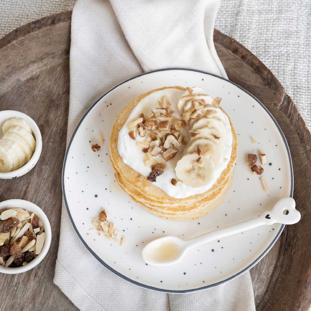 Ein Teller Pfannkuchen mit Schlagsahne und Nüssen von Bastion Collections - Desserteller Herz kleine schwarze Punkte.