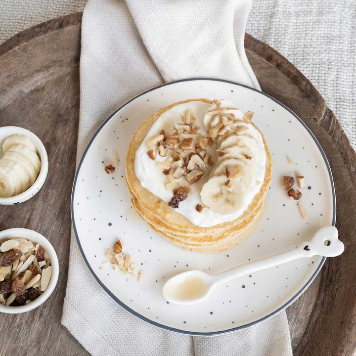 Ein Teller Pfannkuchen mit Schlagsahne und Nüssen von Bastion Collections - Desserteller Herz kleine schwarze Punkte.