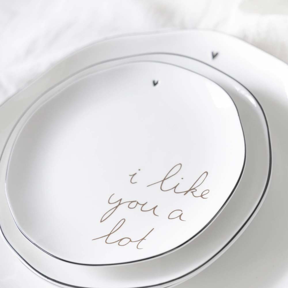 Nahaufnahme von zwei weißen Keramiktellern mit schwarzem Rand und schlichtem Herzdesign von Bastion Collections. Der größere Teller mit dem Namen „Kuchenteller I Like you a lot“ trägt die Aufschrift „i like you a lot“ in Schreibschrift.