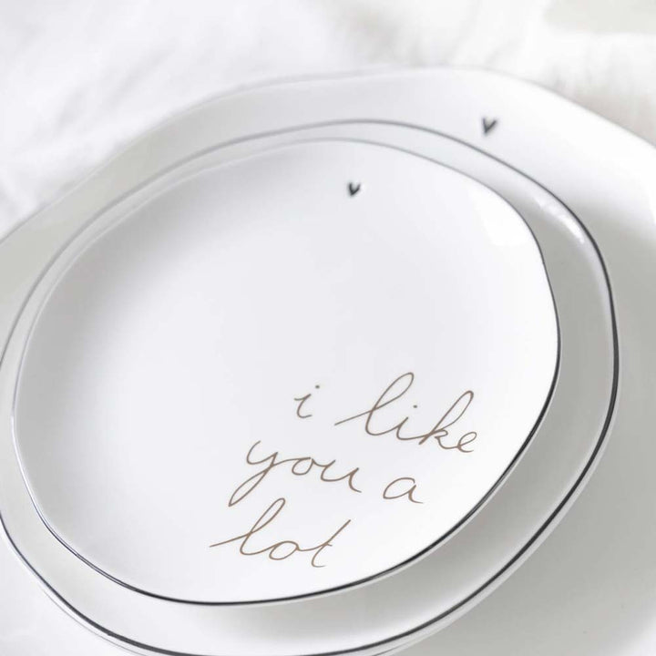 Nahaufnahme von zwei weißen Keramiktellern mit schwarzem Rand und schlichtem Herzdesign von Bastion Collections. Der größere Teller mit dem Namen „Kuchenteller I Like you a lot“ trägt die Aufschrift „i like you a lot“ in Schreibschrift.
