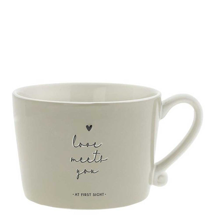 Die Bastion Collections - Tasse Love meets you Titane ist eine cremefarbene Keramiktasse mit Henkel, die auf der Vorderseite den Spruch Love meets you at first sight" und ein kleines Herz zeigt.