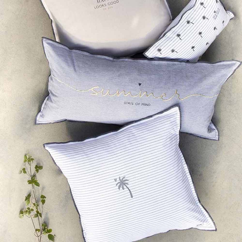 Eine Kollektion dekorativer Kissen mit Sommermotiven auf neutraler Oberfläche. Auf einem Kissen steht „Summer State of Mind“, auf einem anderen sind kleine Palmenaufdrucke zu sehen und auf einem ist der Kissenbezug „Bastion Collections – Palm Tree“ 50 x 50 cm abgebildet.