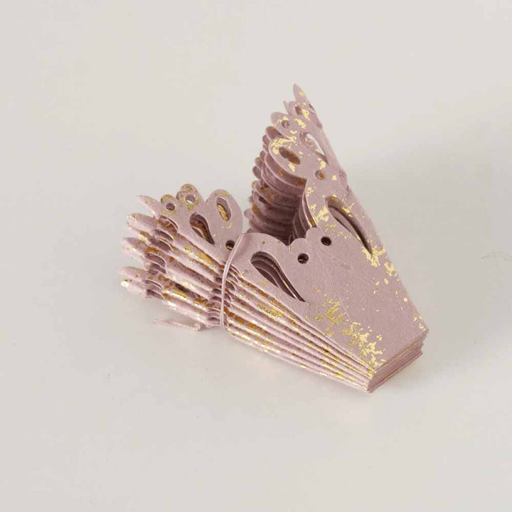 Eine Sammlung rosafarbener, kronenförmiger Papierdekorationen mit goldenen Sprenkeln auf einer hellgrauen Oberfläche.