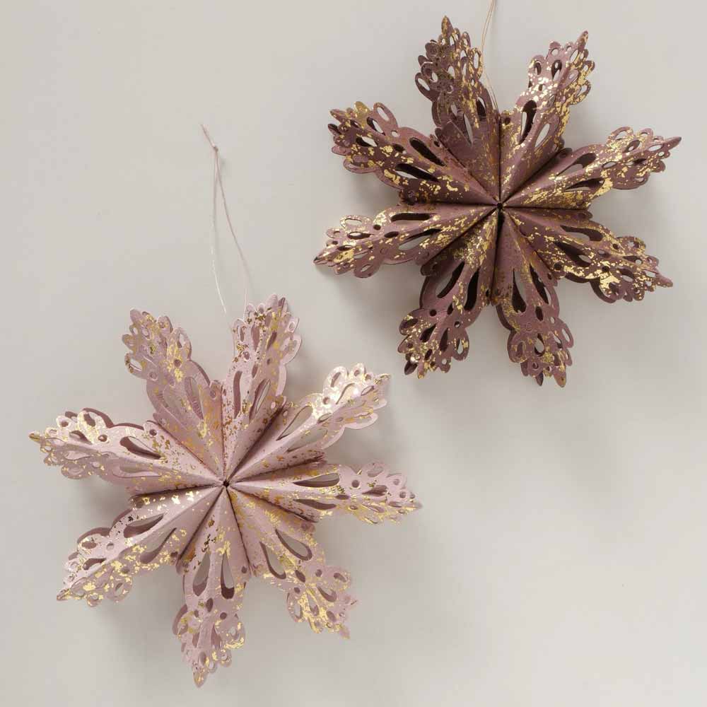 Zwei 3D-Schneeflocken von Boltze mit komplizierten ausgeschnittenen Mustern in Rosa- und Brauntönen mit goldenen Sprenkeln, hängen vor einem hellen Hintergrund.