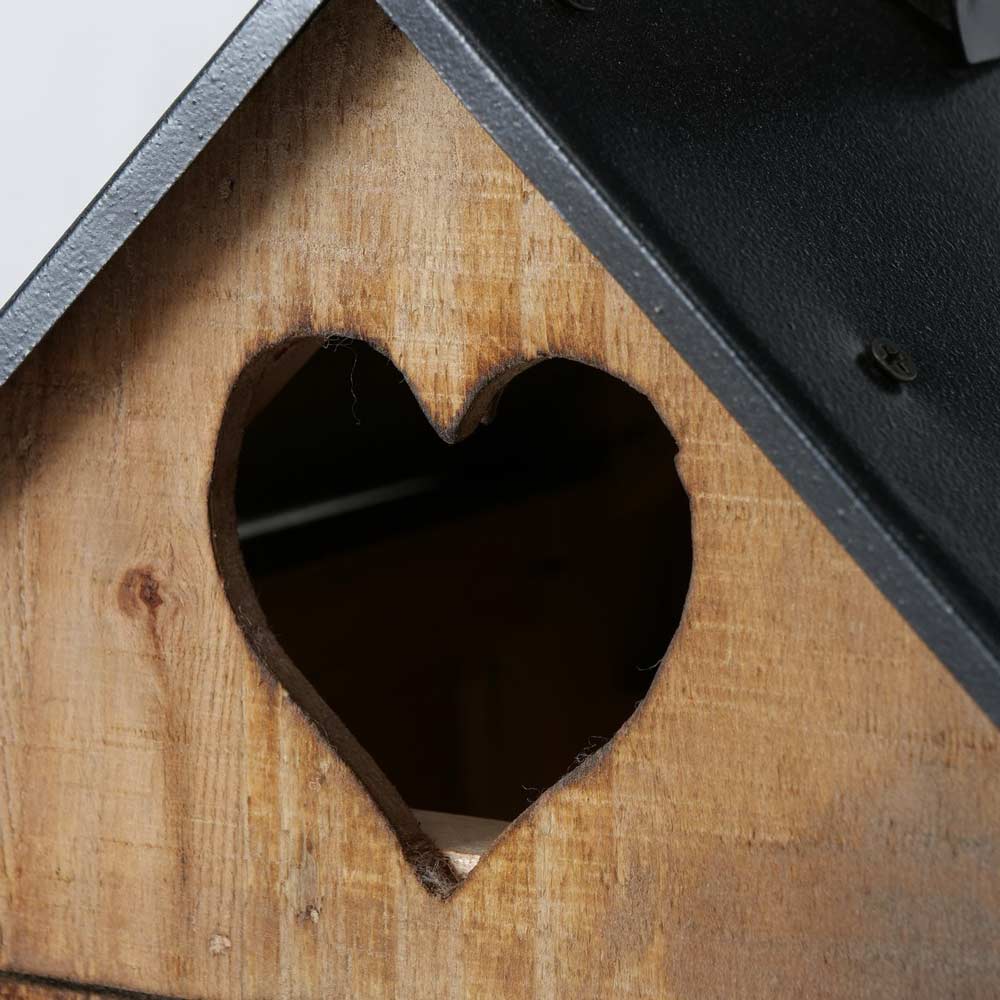 Nahaufnahme des Boltze – Laterne Brixen Haus, mit einer Holzwand mit einer herzförmigen Öffnung und einem schwarzen Dach im Hintergrund.