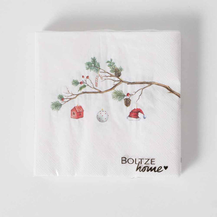 Papierserviette „Weihnacht mit Tannenzweig“ von Boltze, eine weiße Serviette mit einem Baumzweig-Design, das Abbildungen eines kleinen Hauses, einer Weihnachtskugel, einer Zuckerstange, Tannenzapfen und einer Weihnachtsmannmütze enthält. In der Ecke ist der Satz „Boltze home“ aufgedruckt.