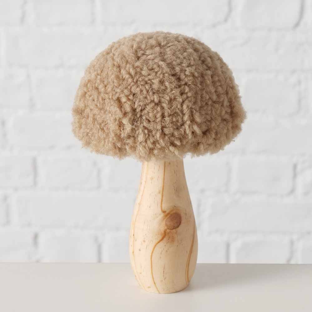 Der Boltze - Pilz Deko Teddy ist ein Holzstück mit einer runden, flauschigen Oberseite, die an lockiges Haar erinnert und sich wunderschön vor einer weißen Backsteinwand abhebt.