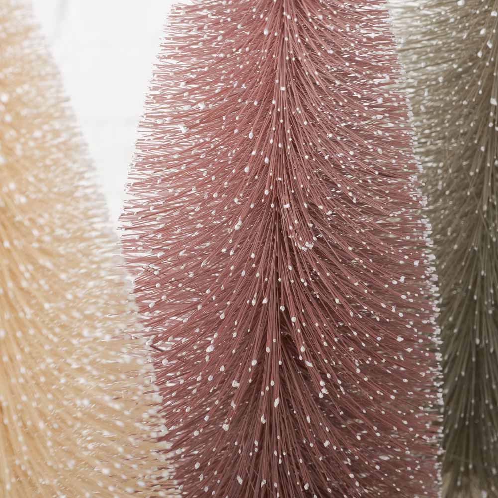 Nahaufnahme von drei Weihnachtsbaumen „Vintage Pastell“ von Boltze in den Farben Beige, Rosa und Grün mit kleinen weißen Flecken, die an Schnee erinnern. Alle stehen auf Holzsockeln und sind 40 cm hoch.