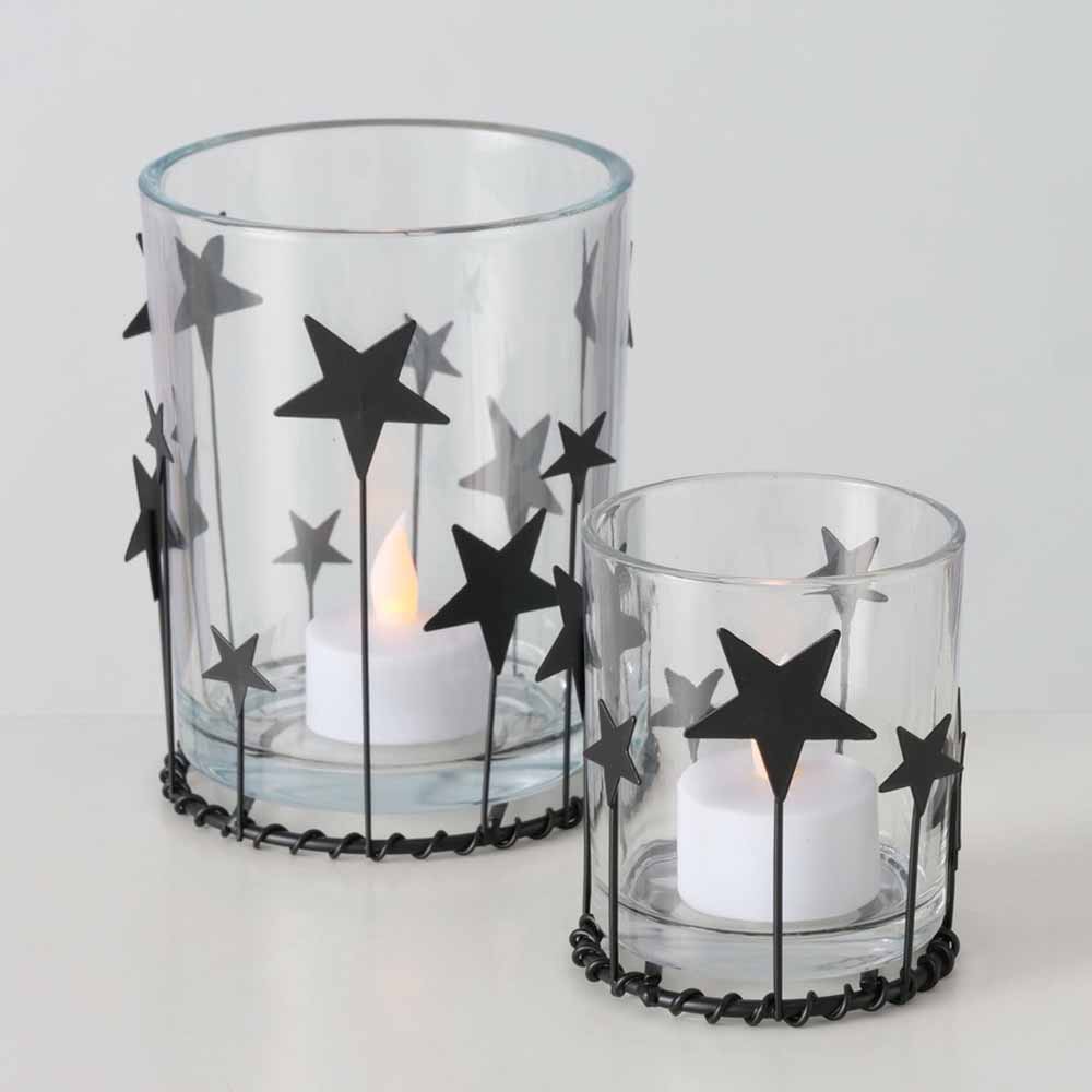 Zwei Boltze - Windlicht Starshine Rund Kerzenständer mit schwarzem Sterndekor, bestückt mit je einem LED-Teelicht, stehen nebeneinander auf einer weißen Fläche.