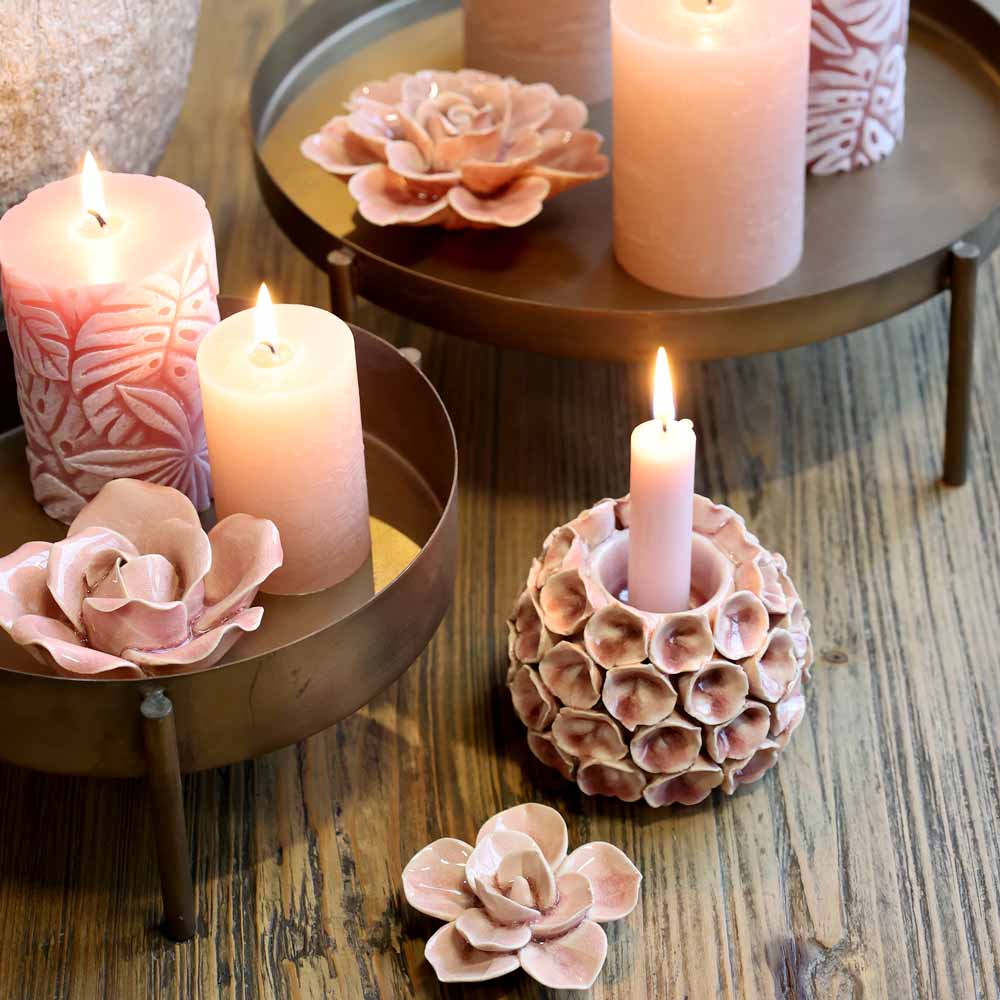 Eine Sammlung brennender rosa Kerzen und Chic Antique – Blume Deko aus Keramik auf runden, erhöhten Tabletts auf einer Holzoberfläche.