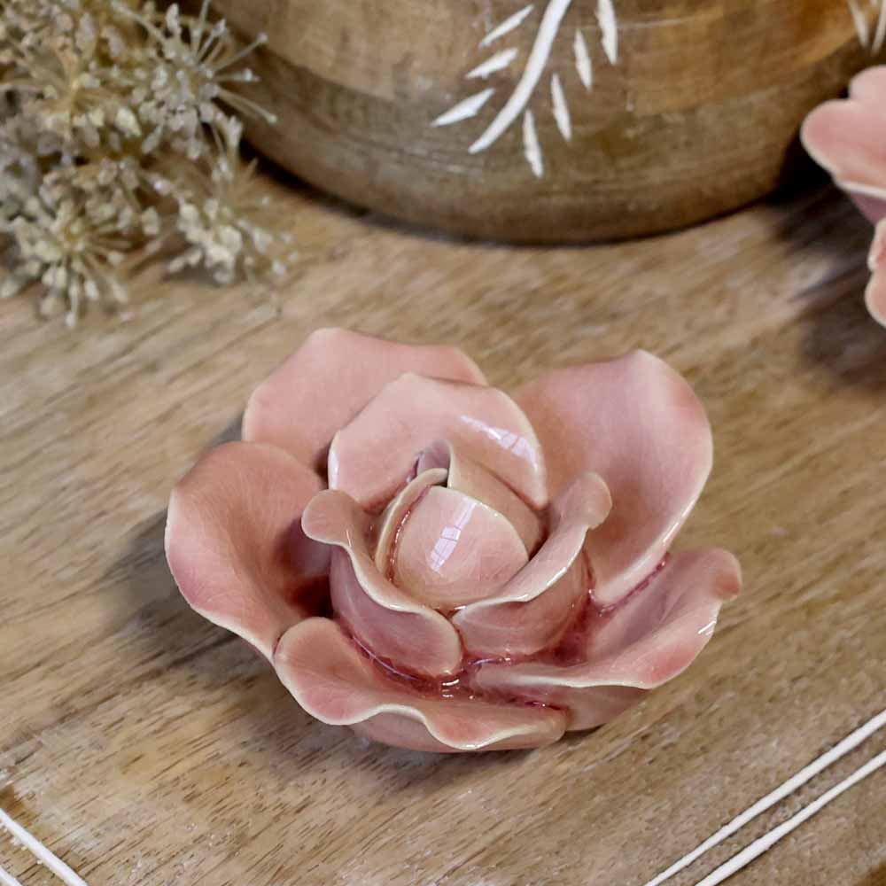 Eine Chic Antique - Blume Deko aus Keramik auf einer Holzoberfläche, mit getrockneten Blumen und einem mit weißen Mustern verzierten Holzgegenstand im Hintergrund.