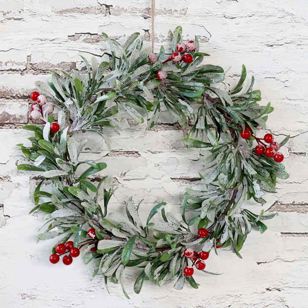 Der Chic Antique – Fleur Kranz mit Schnee und Beeren 37 cm wird vor einer weißen Backsteinwand ausgestellt.