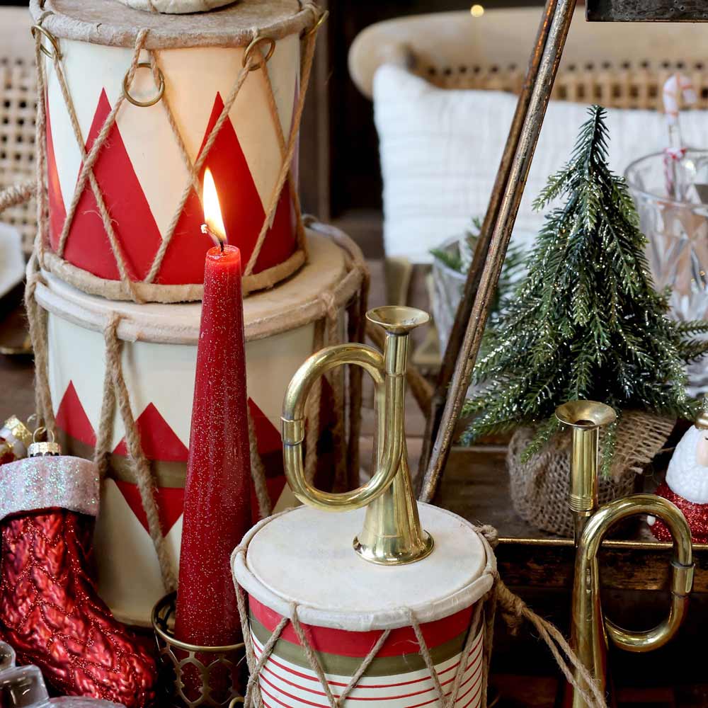 Festliche Dekoration mit einer brennenden roten Kerze, roten und weißen Trommeln, einem Messinghorn, einem Chic Antique - Fleur Tannenbaum mit glitzergoldenem Tannenbaum und einem roten Strumpf.
