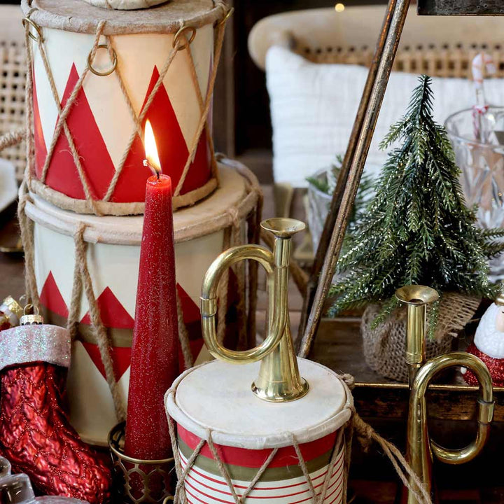 Festliche Dekoration mit einer brennenden roten Kerze, roten und weißen Trommeln, einem Messinghorn, einem Chic Antique - Fleur Tannenbaum mit glitzergoldenem Tannenbaum und einem roten Strumpf.