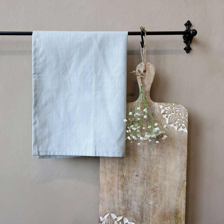 Das Chic Antique - Geschirrtuch Maritimes Streifenmuster, ein hellblau gestreiftes Tuch, hängt an einer schwarzen Wandstange neben einem hölzernen Schneidebrett mit weißem Blumenmuster und einem Strauß weißer Blumen.