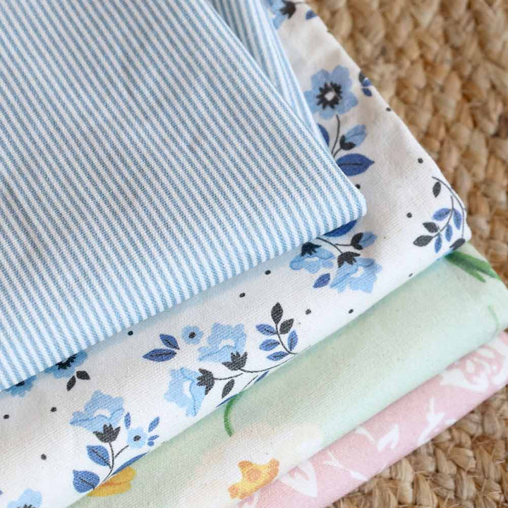 Ein Chic Antique Geschirrtuch „Maritimes Streifenmuster“, gefaltet und gestapelt mit zwei anderen gemusterten Stoffen – blauen Blumen und pastellfarbenen Blumenmustern – liegt auf einer gewebten Oberfläche.