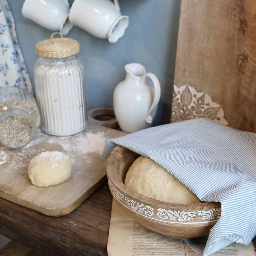 Auf einem Tisch steht eine Schüssel mit Teig, bedeckt mit dem Chic Antique - Geschirrtuch Maritimes Streifenmuster, neben einer kleineren Teigkugel, einem Glas Mehl, einem Krug und darüber hängenden Tassen.