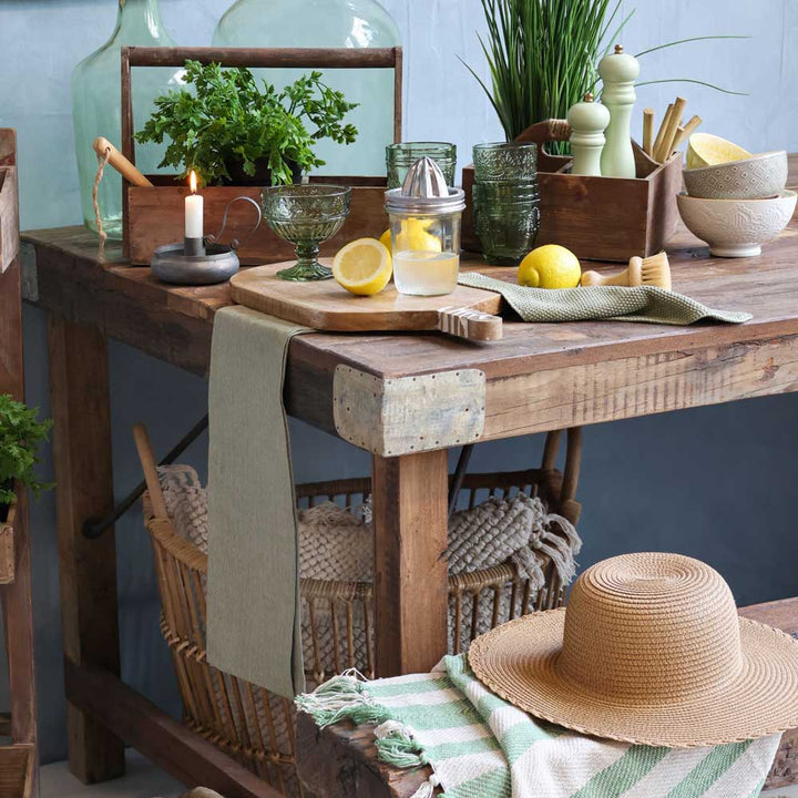 Rustikale Küchenszene mit der Henkelbox mit drei Fächern von Chic Antique auf einem Holztisch, umgeben von Zitronen, einer Saftpresse, einer brennenden Kerze, Kräutertöpfen, Glaswaren, einem Strohhut und einem Korb darunter.