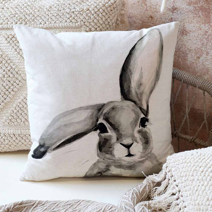 Ein Leinenkissenbezug von Chic Antique, „Kissenbezug mit Hase Männchen“, mit der Skizze eines Hasenkopfes ziert einen Stuhl, der von gestrickten Decken umgeben ist.