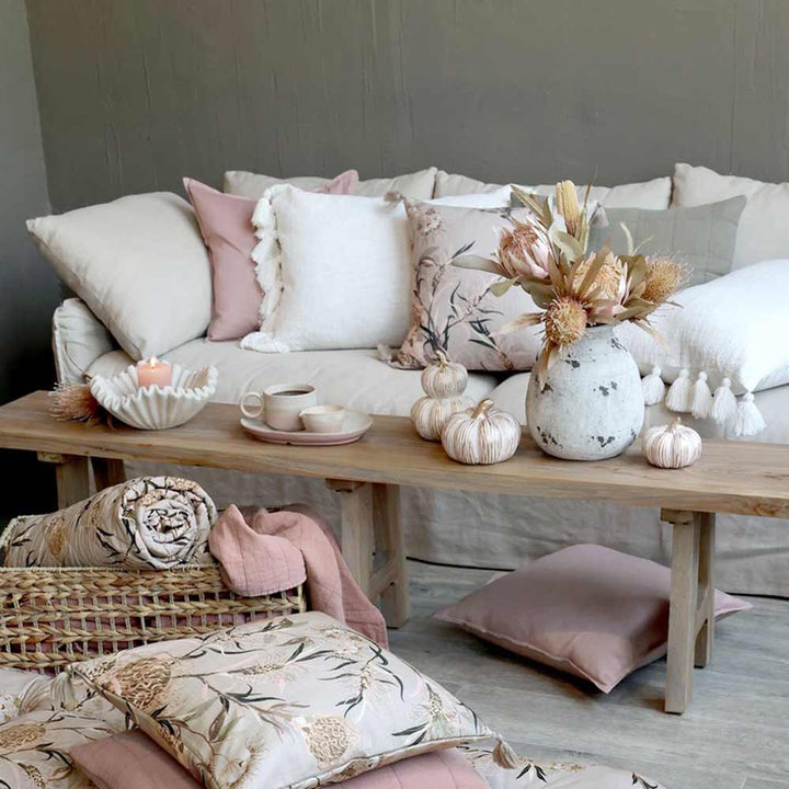 Ein gemütliches Wohnzimmer mit einem neutralen Sofa, verschiedenen Kissen, einem hölzernen Couchtisch mit Trockenblumen und dem Chic Antique Kürbis mit Gold Antique Creme sowie einem Korb mit gefalteten Decken und Kissen.
