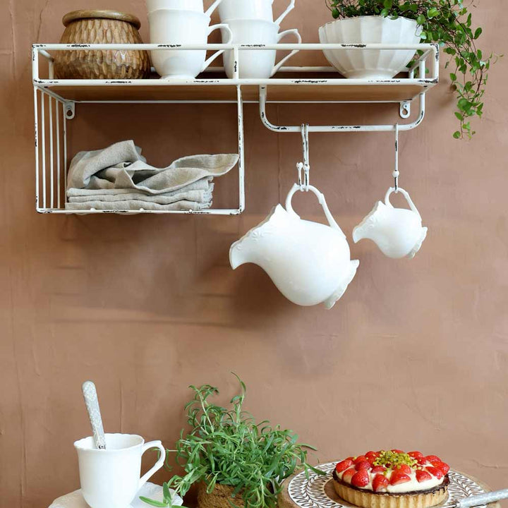 Ein Küchenregal mit weißem Keramikgeschirr und einer Pflanze. Darunter eine Tischplatte mit einer Erdbeertorte, einer Pflanze, einer Tasse und Chic Antique - Provence Milchkännchen.