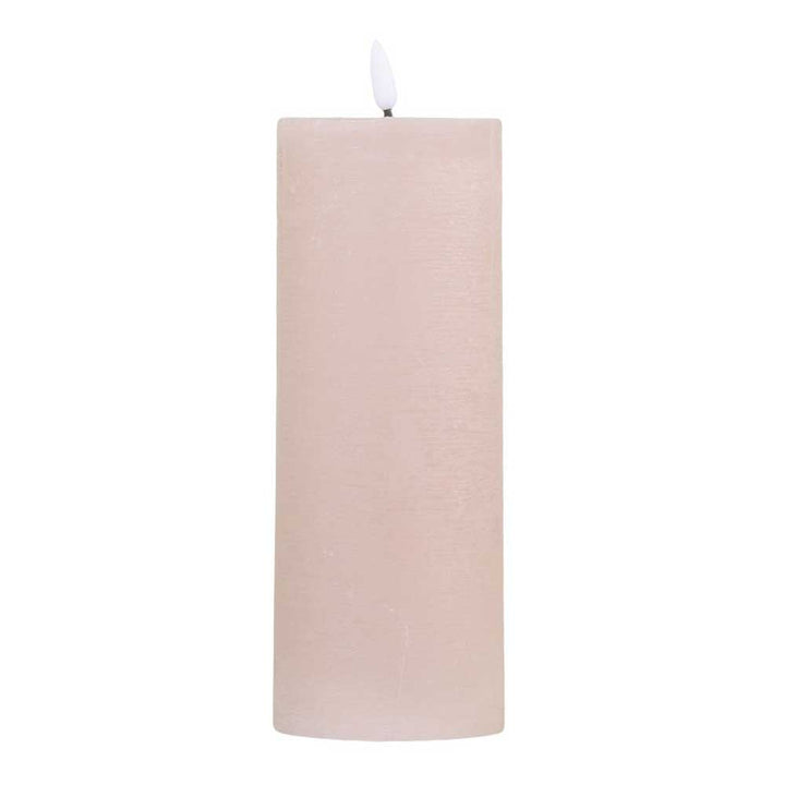 Eine große, zylindrische, beige Chic Antique - Stumpenkerze LED staubig rosa inkl. Batterie mit einer brennenden weißen Flamme.