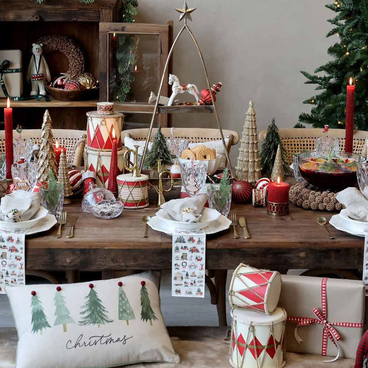 Ein festlicher Feiertagstisch ist mit rot-weißen Dekorationen geschmückt, mit schickem Kerzenlicht von Chic Antique – Stumpenkerze mit Rillen und Glitzer sowie weihnachtlich gestaltetem Geschirr. Geschenke und ein Weihnachtsbaum ergänzen die Szene im Hintergrund wunderschön.