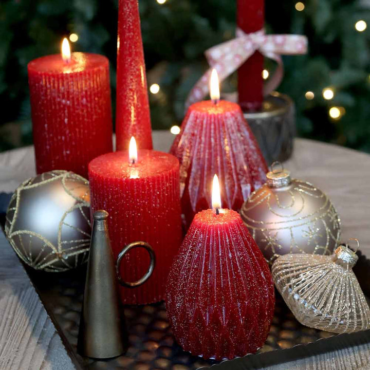 Auf dem Tablett ist Chic Antique – Stumpenkerze mit Rillen und Glitzer neben dekorierten Ornamenten zu sehen, im Hintergrund ist ein Weihnachtsbaum zu sehen.