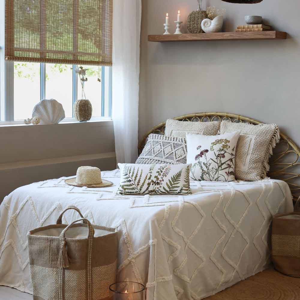 Ein sanft beleuchtetes Zimmer verfügt über ein ordentlich gemachtes Bett mit dekorativen Kissen, einer Decke, Bambusjalousien am Fenster, geflochtenen Körben, Akzenten im Küstendekor und der Chic Antique – Vase Muschel, die einen Hauch von Eleganz verleiht.