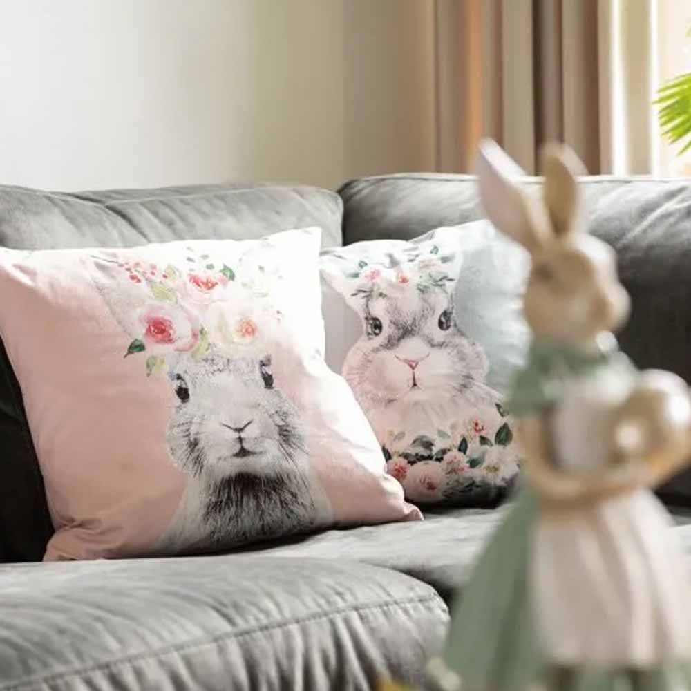 Zwei dekorative Kissen mit Clayre & Eef – Kissenbezug Hase mit Blumen Samt rosa Designs auf einem Sofa.