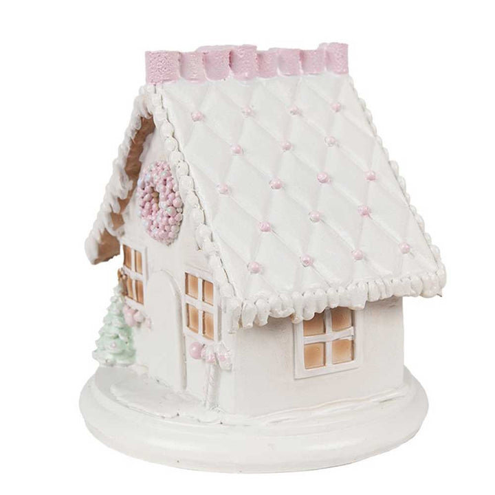 Ein charmantes, kompaktes weißes Dekohaus mit rosa Dach, mit Steppmuster und zarten Pastellakzenten verziert. Das Clayre & Eef - Lebkuchenhaus mit LED 13 cm ruht auf einem runden Sockel.