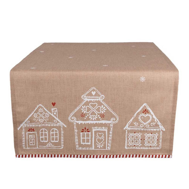 Eine beige Tischdecke von Clayre & Eef namens „Tischläufer Lebkuchenhäuser“, mit weiß-roten Dekormustern von drei Häusern auf der einen Seite.
