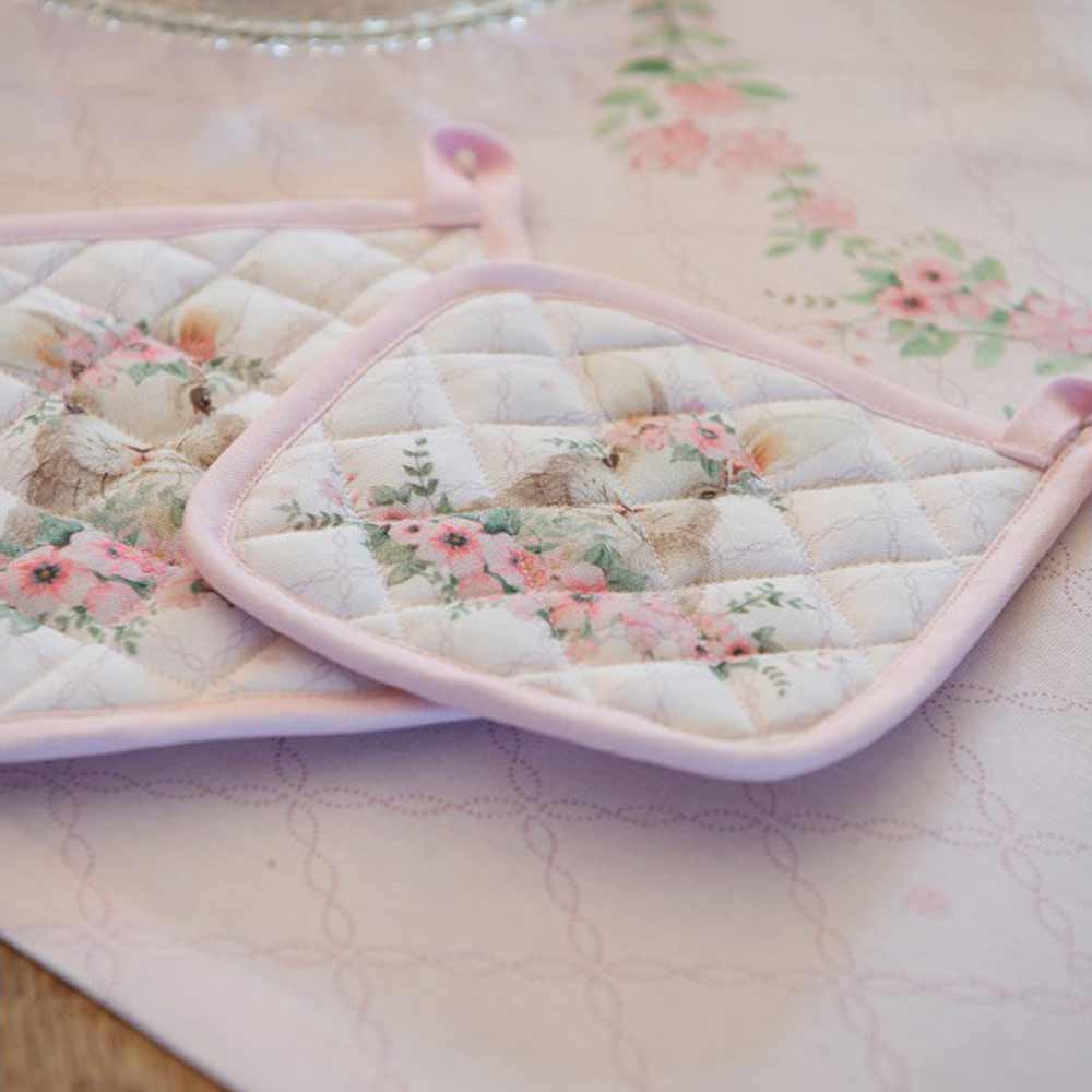 Zwei Clayre & Eef - Ofenhandschuh Hase Rosa auf einem Tisch mit Blumen darauf.