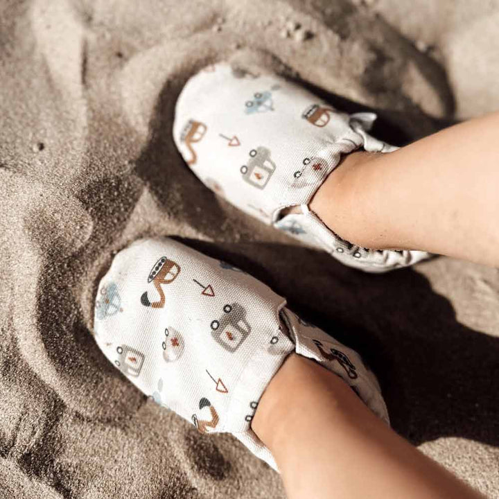 Kinderfüße in Cozy Roots - Lauflernschuhe Little Driver auf sandigem Untergrund.