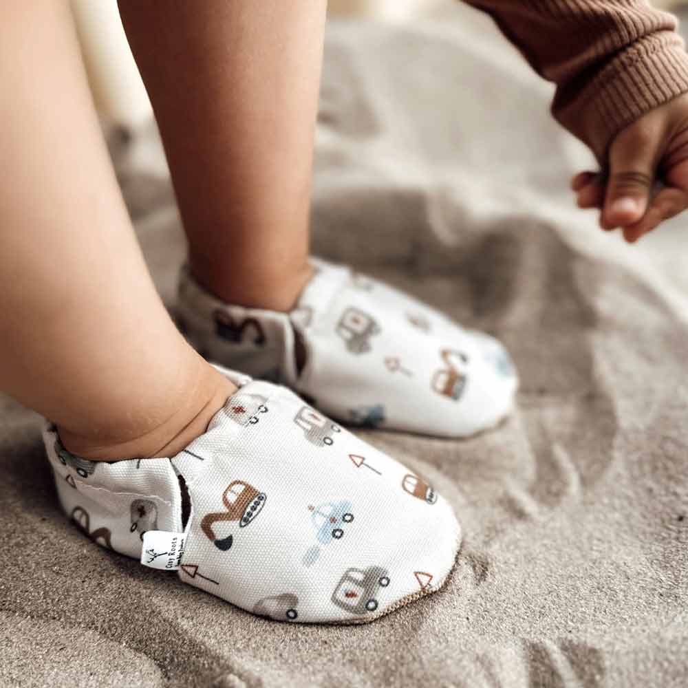 Ein Kind in Cozy Roots - Lauflernschuhen Little Driver greift nach einem nahegelegenen Gegenstand.