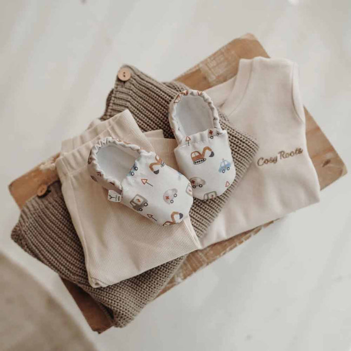 Ein Set aus Babykleidung und Cozy Roots – Lauflernschuhen Little Driver mit einer neutralen Farbpalette.