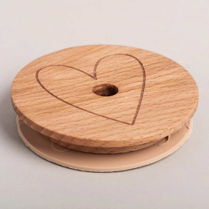 Der Eulenschnitt - Deckel Herz für Hohes Trinkglas ist ein runder Holzdeckel mit einer Herzgravur oben, einem zentralen Loch und einem beigen Kunststoffboden, der für hohe Trinkgläser geeignet ist.
